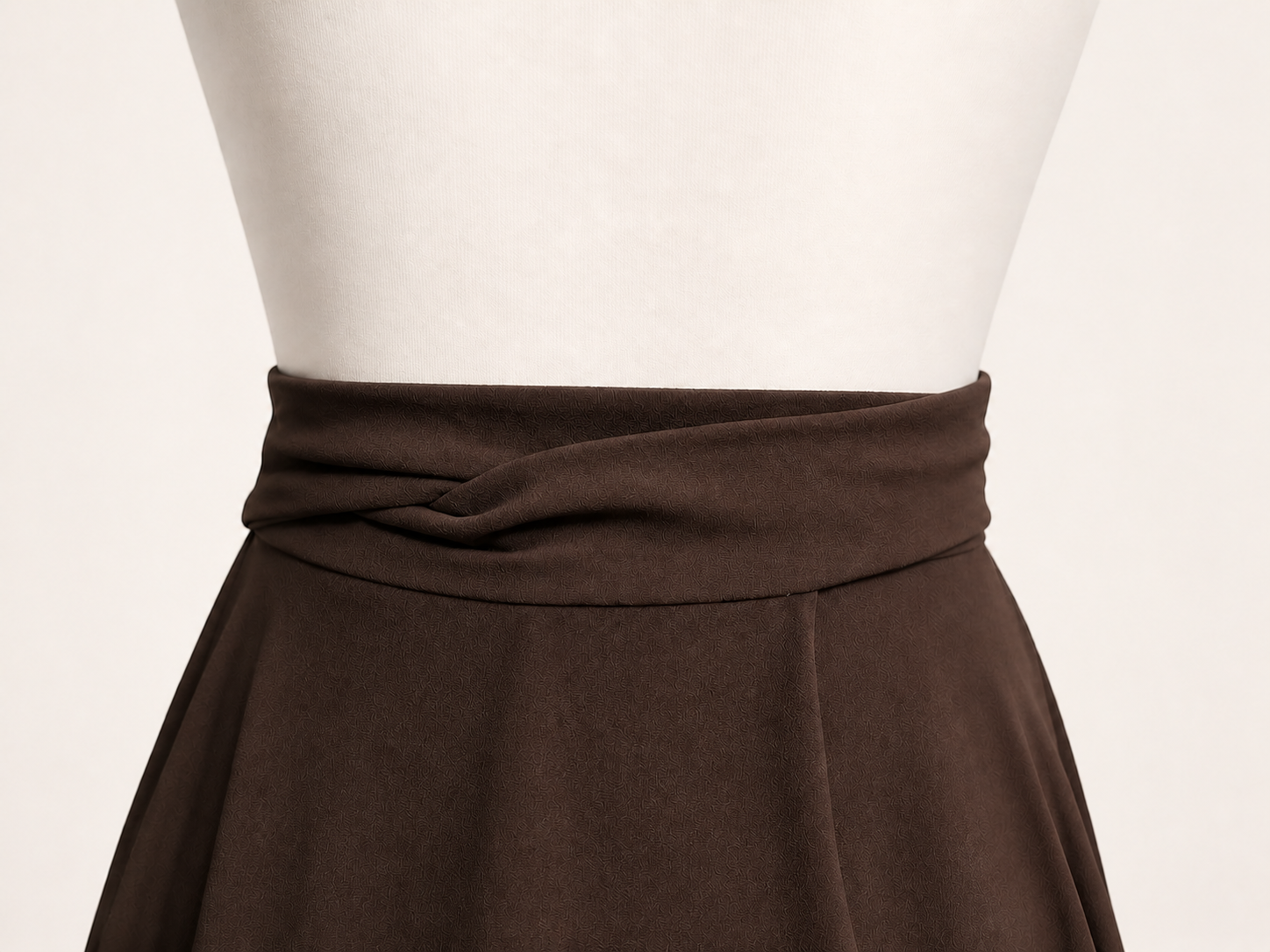 Detalle de las cintas cruzadas de una saya marrón oscuro sobre un maniquí blanco